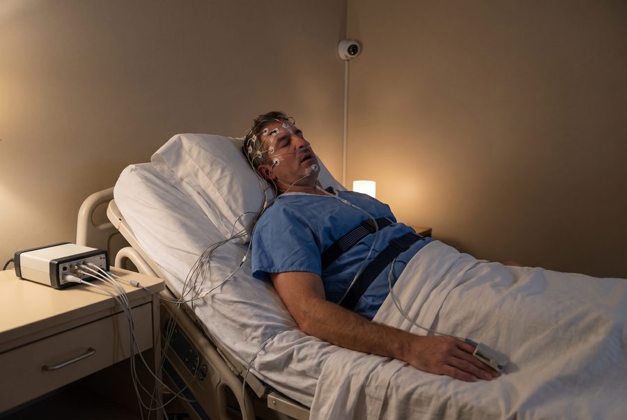 His overnight sleep study at a sleep clinic: wires on his head and face, belts on his chest, a sensor on his finger