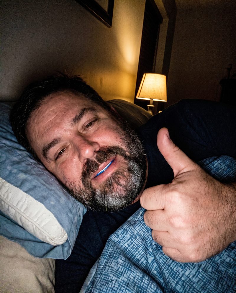 A husband in bed wearing it with his lips closed, thumbs up
